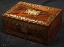 JB507: Rosewood box inlaid with brass to the front and top depicting stylized flora.  The design is controlled in deference to the Georgian neo-classical tradition but it also embraces the Regency influence of the Royal cabinet maker George Bullock, who introduced naturalistic elements to the earlier austere brass designs.  The inside of the box has been relined with hand marbled paper and velvet  and retains  its original lift out tray.  Circa 1825. Enlarge Picture