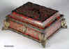 A shaped casket covered in boulle work of brass and red tortoiseshell,  with guilt ormolu mounts and feet. The pattern is in bold swirls forming floral designs and cusps typical of 18th century work.  The brass is engraved to give dimension to the design. The top is built around a stage where a musician sits playing his instrument. A complex composition, opulent and at the same time whimsical. The box is lined with silk.  Circa 1750 Enlarge Picture